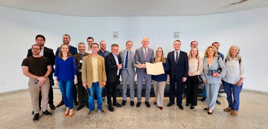 Pessoas em pé com um documento histórico aberto pousando para foto