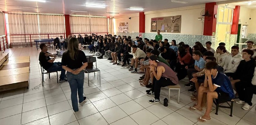 TRE-SC-Ação-de-cidadania-Laguna Imagem de um evento em uma escola pública em Laguna/SC com vários alunos sentados em um pátio.