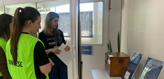 Eleitoras observando a urna de madeira em exposição de peças do museu do TRE-SC na Unoesc Day